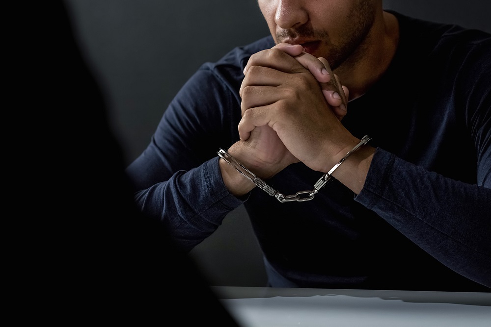 Criminal with handcuffs in interrogation room feeling guilty after committed a crime.