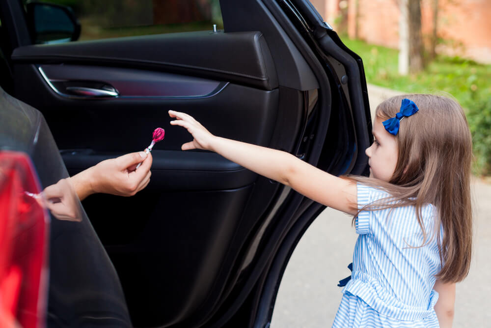 Stranger luring young girl by giving her lollipop to get in the car.