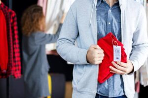 Closeup of young man is stealing red jeans in store.